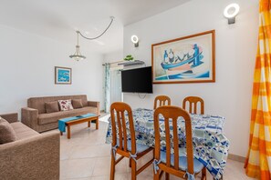 Un salon comprenant un canapé, une table basse, une table à manger avec des chaises, un téléviseur à écran plat et des œuvres d’art accrochées au mur.