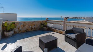 A rooftop terrace with a view of the sea, wicker furniture, and potted plants.