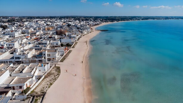 An aerial view of a coastal town with a beach, white buildings, and clear blue waters.