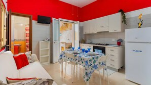 A compact living space with a kitchenette, a dining area with a table set for two, and a sofa with a red pillow.