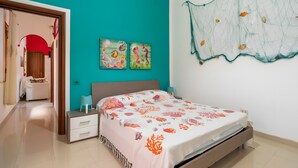 A bedroom with a teal wall, a bed with a coral-patterned bedspread, two wall art pieces, and a net decoration.