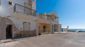 A multi-story residential building with balconies, a stone facade, and a view of the sea.