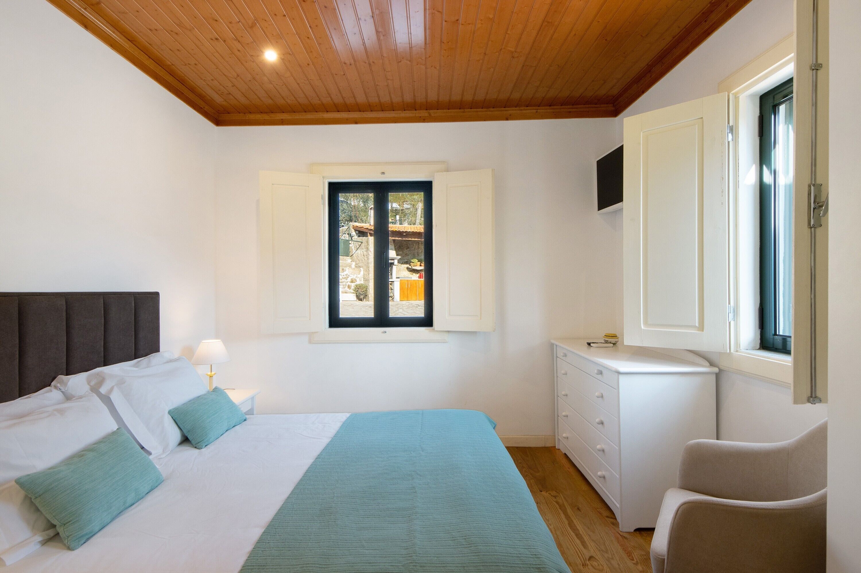A bedroom with a bed, a nightstand, a dresser, a chair, and a window with shutters.