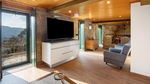 Una sala moderna con un televisor de pantalla plana grande, paredes de piedra, techo de madera y vistas al exterior.
