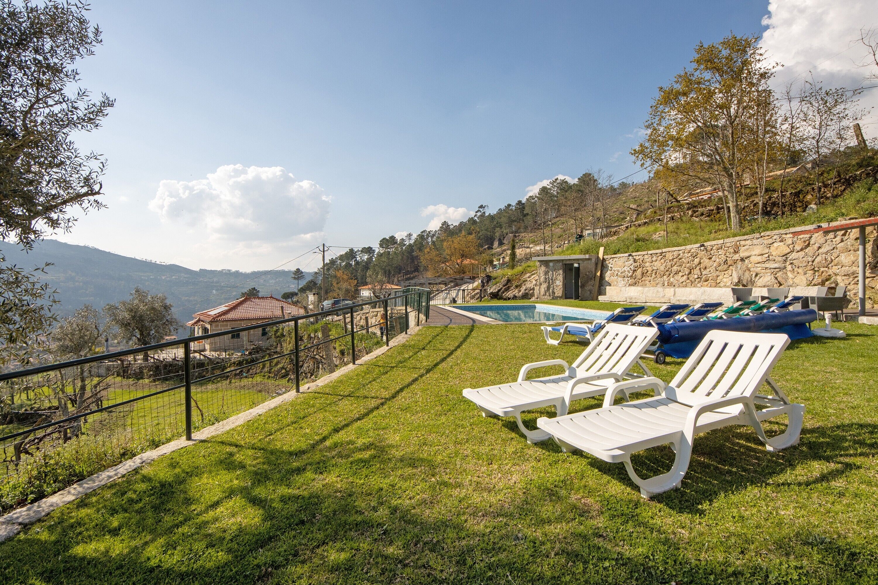 Zona de piscina con sillones de descanso, un muro de piedra y vistas a las montañas.
