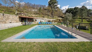 Una piscina con sillas de descanso, un muro de piedra y un área con césped.