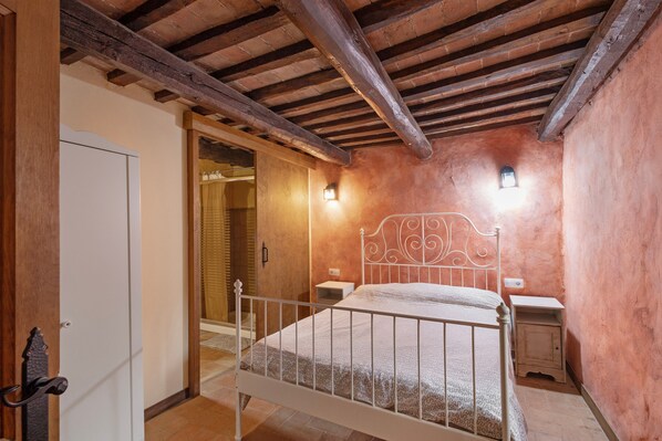 Un dormitorio con estructura de cama de metal, puerta de madera, una mesita de noche pequeña y un aplique de pared.