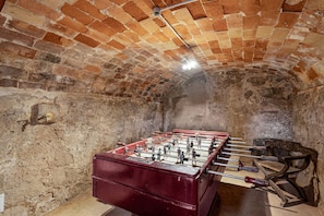 A room with a foosball table, brick walls, and a stone floor.