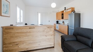 A modern kitchen with wooden cabinets, a central island, a black sofa, and a pendant light.