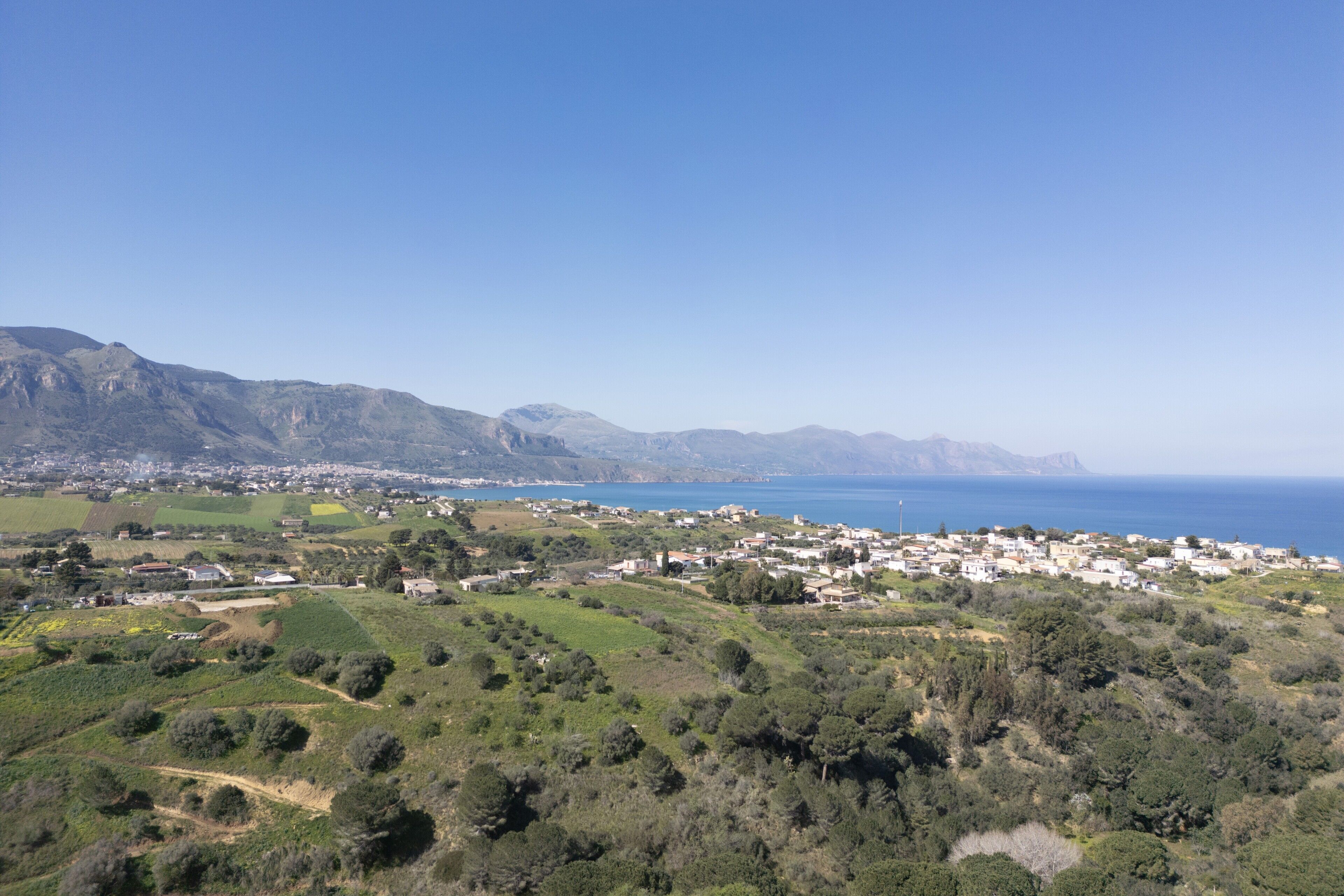 A coastal town with a hilly landscape, a clear sky, and a view of the sea.