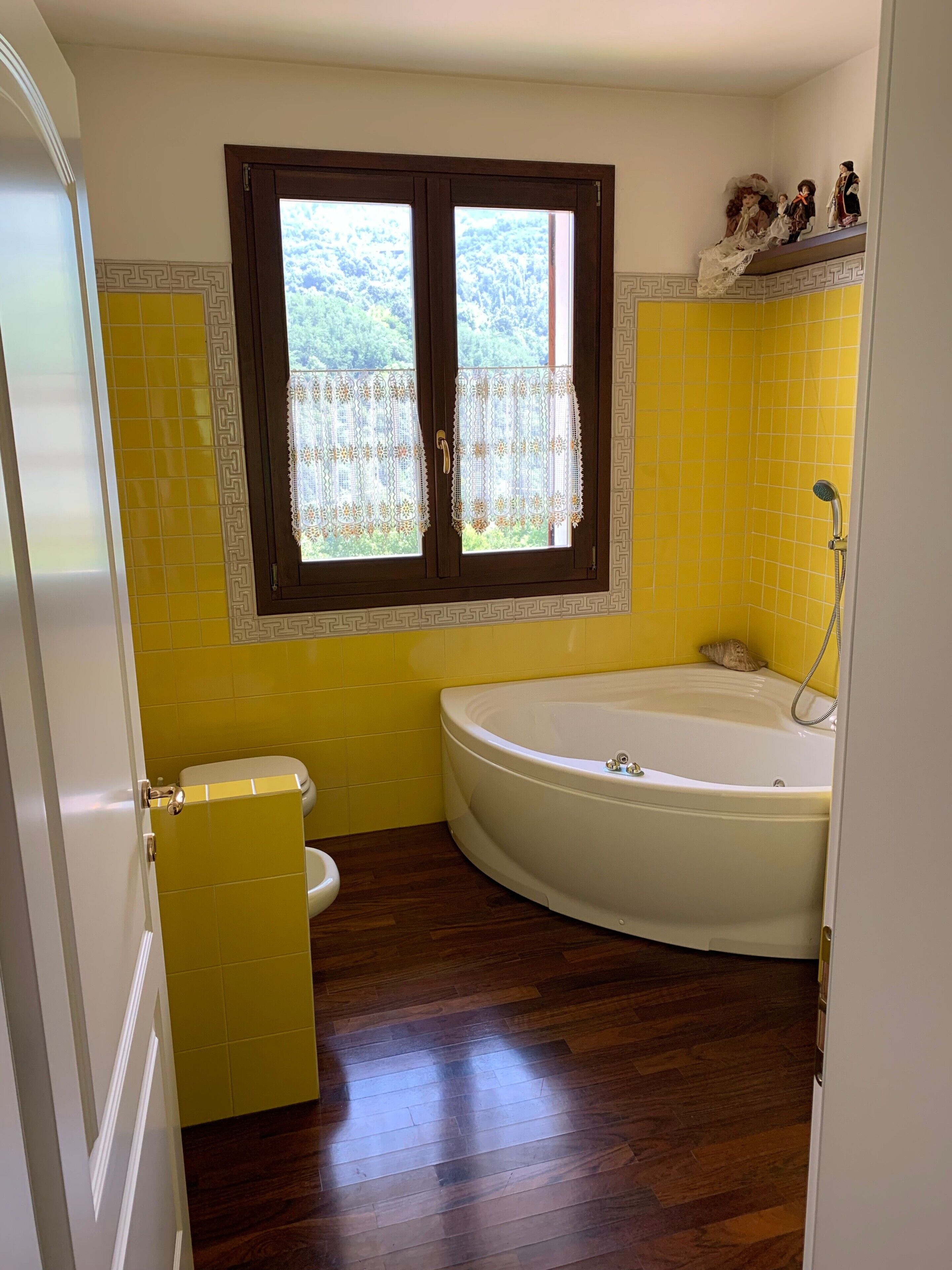 A bathroom with a bathtub, toilet, and window with lace curtains.