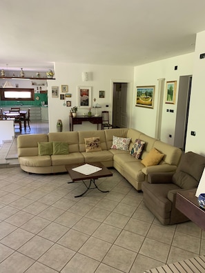 A living room with a beige sectional sofa, a coffee table, and a dining area with a table and chairs. - Villa 'Casa Di Eli E Matte' with Mountain View, Private Garden and Wi-Fi (Cà D'onofrio)