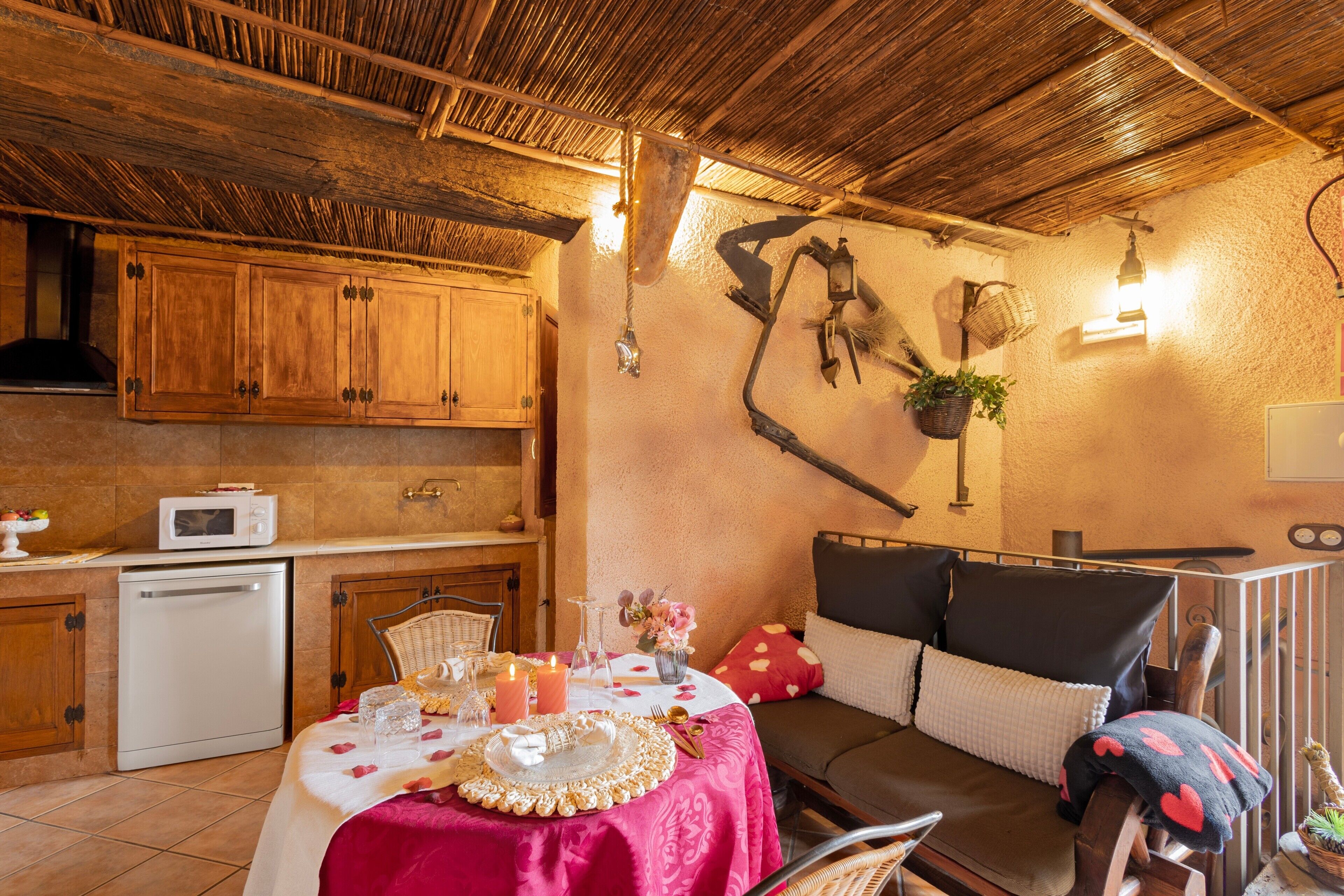 A cozy kitchen with wooden cabinets, a dining table set with a pink tablecloth, and a seating area with a sofa and chairs.