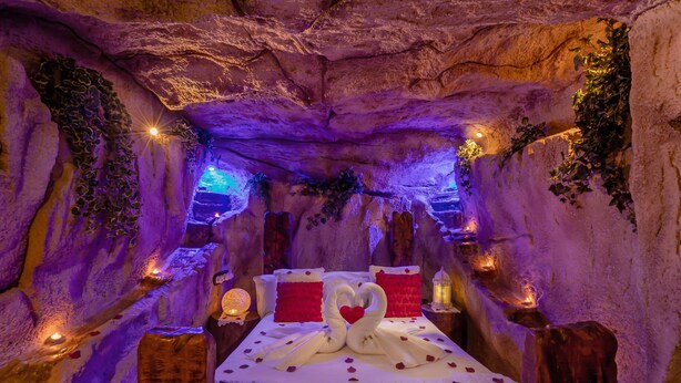 A cave-themed bedroom with a bed, pillows, and decorative elements like flowers and plants.