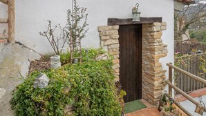 A rustic building with a stone entrance, a wooden door, and a small porch area with a lantern.