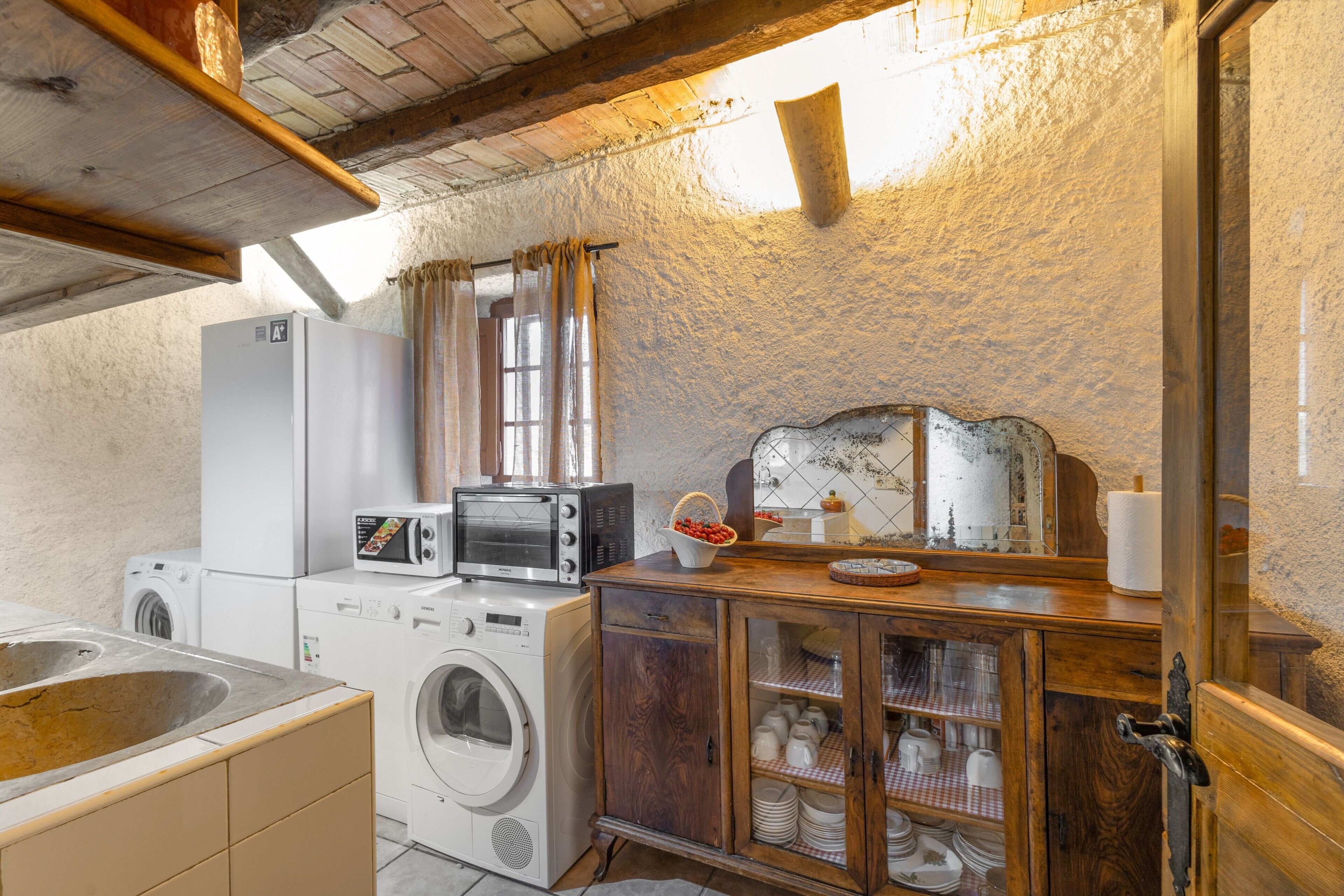 Une cuisine compacte équipée d’un lave-linge, d’un four à micro-ondes, d’un grille-pain et d’un meuble en bois aux portes vitrées.