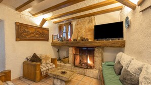 A cozy living room with a stone fireplace, wooden beams, a television, and a fireplace screen. - Chalet 'Can Pavet' with Mountain View, Private Pool and Wi-Fi (Pontons)