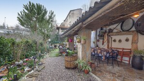 A courtyard with a stone floor, potted plants, outdoor seating, and a rustic building with a sloped roof. - Chalet 'Can Pavet' with Mountain View, Private Pool and Wi-Fi (Pontons)