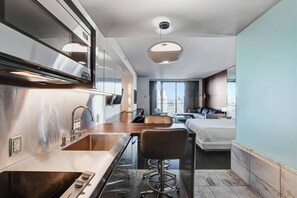 Ein kompaktes Hotelzimmer mit Küchenzeile, Essbereich, einem Bett und einem großen Fenster mit Blick auf die Stadt.