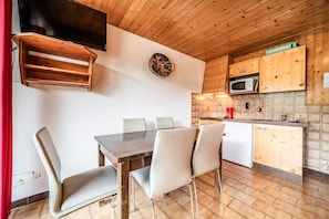 A wooden-paneled room with a dining table, chairs, a TV, and a kitchen area with cabinets and appliances.