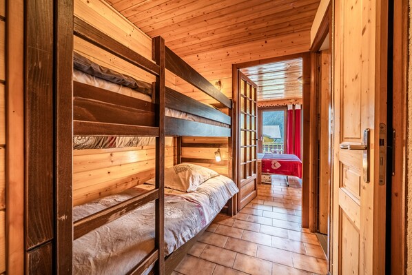 Un intérieur en bois avec des lits superposés, un sol carrelé et une table rouge à l’arrière-plan.