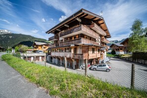 Un edificio de madera de varios pisos con balcones, un estacionamiento y montañas al fondo.