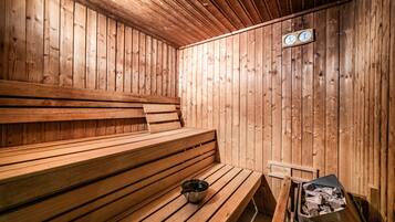 A wooden sauna with benches, a bucket, and a wood-fired stove.