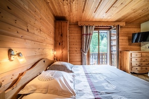 Un dormitorio de cabaña de madera con una cama, un aparador, un televisor y una ventana con cortinas.