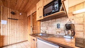 A kitchen with wooden cabinets, a microwave, a coffee maker, and a dishwasher. - Studio Apartment 'Le Blanchot - 4 Pers' with Mountain View, Balcony and Wi-Fi (Châtel)