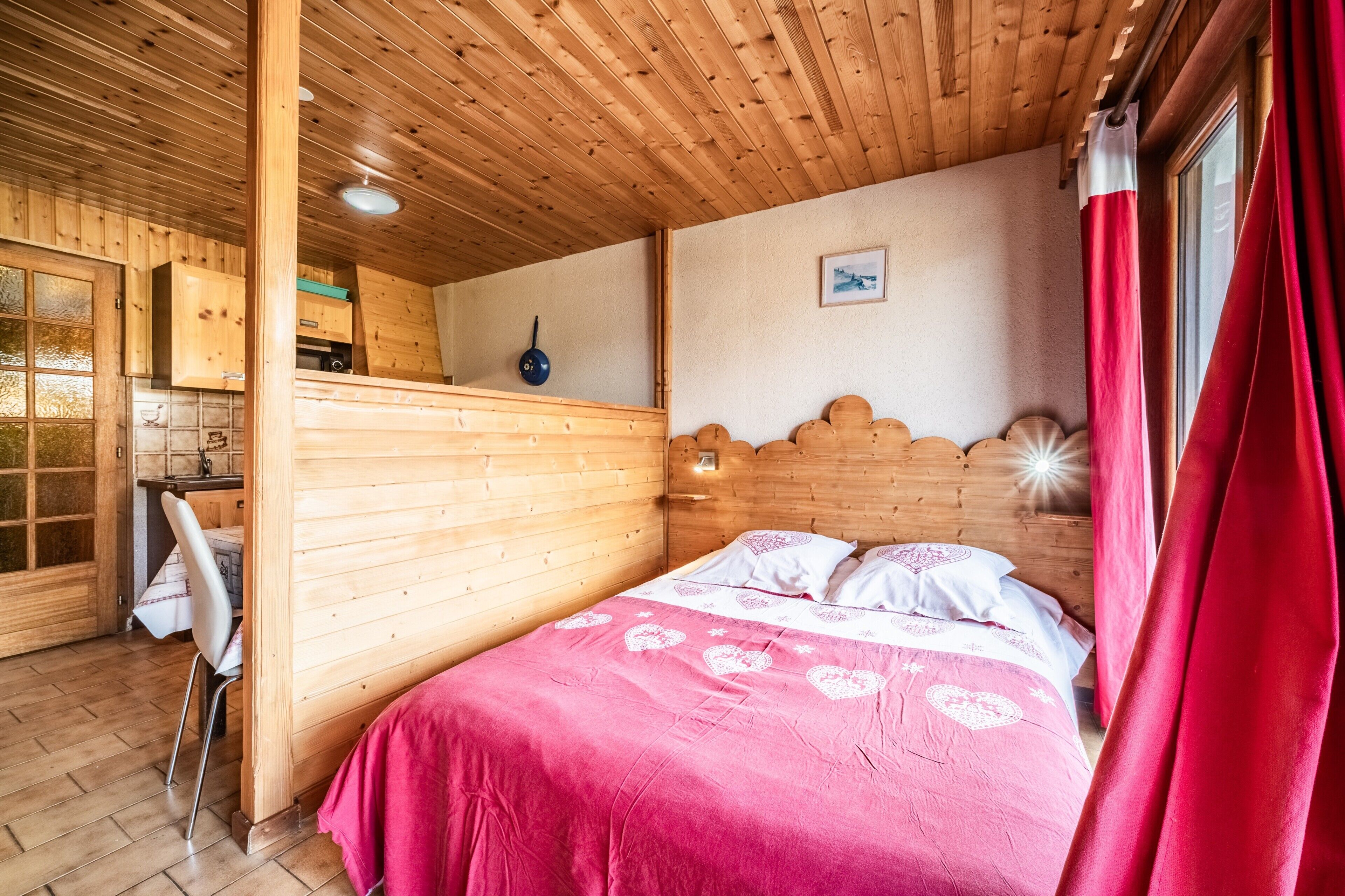 A wooden cabin interior with a bed, a dining area, and a kitchen.