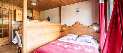 A wooden cabin interior with a bed, a dining area, and a kitchen.