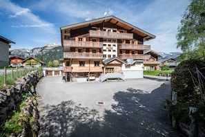A multi-story hotel with balconies, a stone wall, and a mountain backdrop.