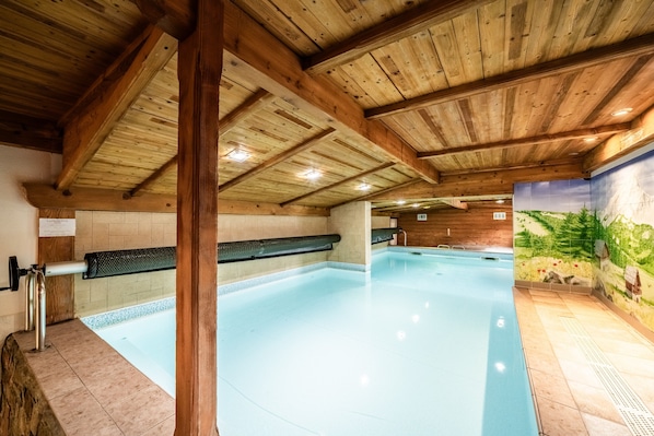 An indoor swimming pool with wooden beams, a tiled wall, and a mural.