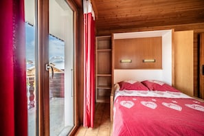 A bedroom with a wooden ceiling, a sliding glass door, a bed with a red bedspread, and a wooden wardrobe.