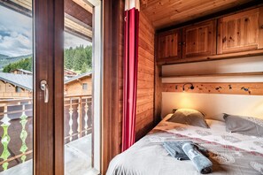 A wooden cabin bedroom with a bed, pillows, and a view of a balcony and forested area.