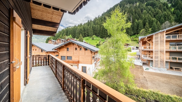 A wooden balcony with a view of a mountain and a village.