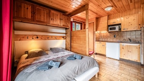 A wooden cabin interior with a bed, a kitchenette, and a window.