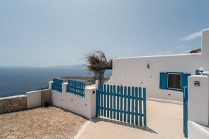 En byggnad vid kusten med en vit fasad och blå detaljer, ett staket och utsikt över havet.