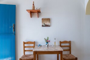 A room with a blue door, a wooden table with chairs, a vase with flowers, a bottle, and a wall-mounted shelf with a bottle and two light switches. - Holiday Home 'Mesaria' with Sea View, Wi-Fi and Air Conditioning (Donousa)
