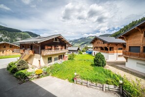A wooden chalet-style building with a balcony, surrounded by a well-maintained garden and a clear view of the mountains in the background. - Apartment 'Le Izzy - 5 Pers' with Mountain View, Balcony and Wi-Fi (Châtel)