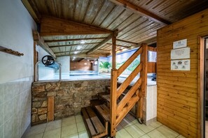 Un escalier en bois menant à une zone abritant une piscine, un mur en pierre et un plafond en bois.