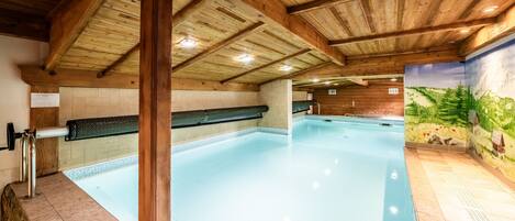 Una piscina interior con vigas de madera, un muro de azulejos y un mural.