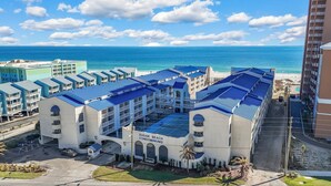A large hotel with multiple blue-roofed buildings, a parking area, and a view of the ocean.