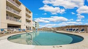 A pool area with lounge chairs, a building with balconies, and a clear blue sky.