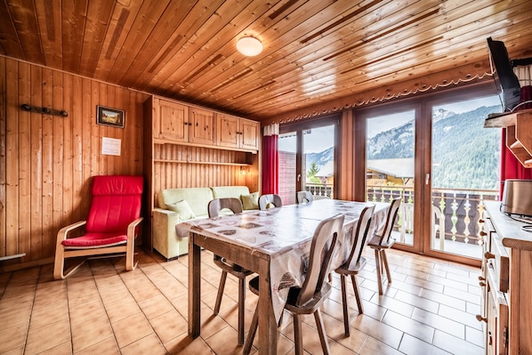 A wooden interior with a dining table, chairs, a red chair, a sofa, and a kitchen area.