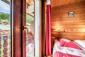 A wooden cabin room with a bed, a window, and a door leading outside.