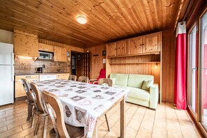 A wooden interior with a dining table, chairs, a sofa, and wooden cabinets.