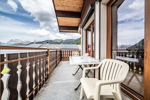 A balcony with a table and chairs, a wooden railing, and a view of mountains.