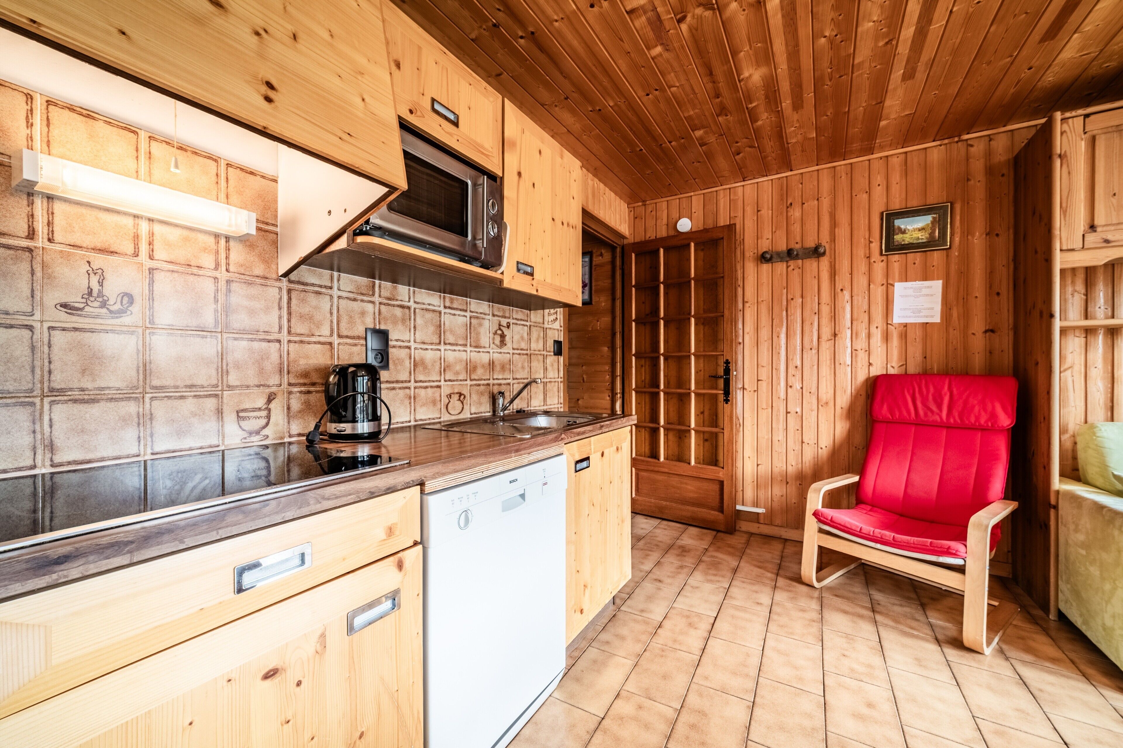 Un intérieur en bois comprenant un coin cuisine équipé d’un lave-vaisselle, d’un four à micro-ondes et d’une chaise rouge.