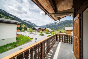 A balcony with a view of a mountain village, wooden buildings, and a paved road.